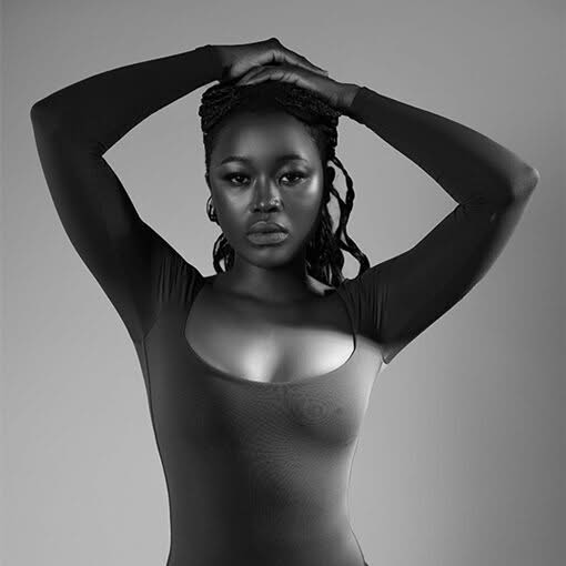 Woman in a fitted sleeveless top posing with both arms raised in a black and white portrait